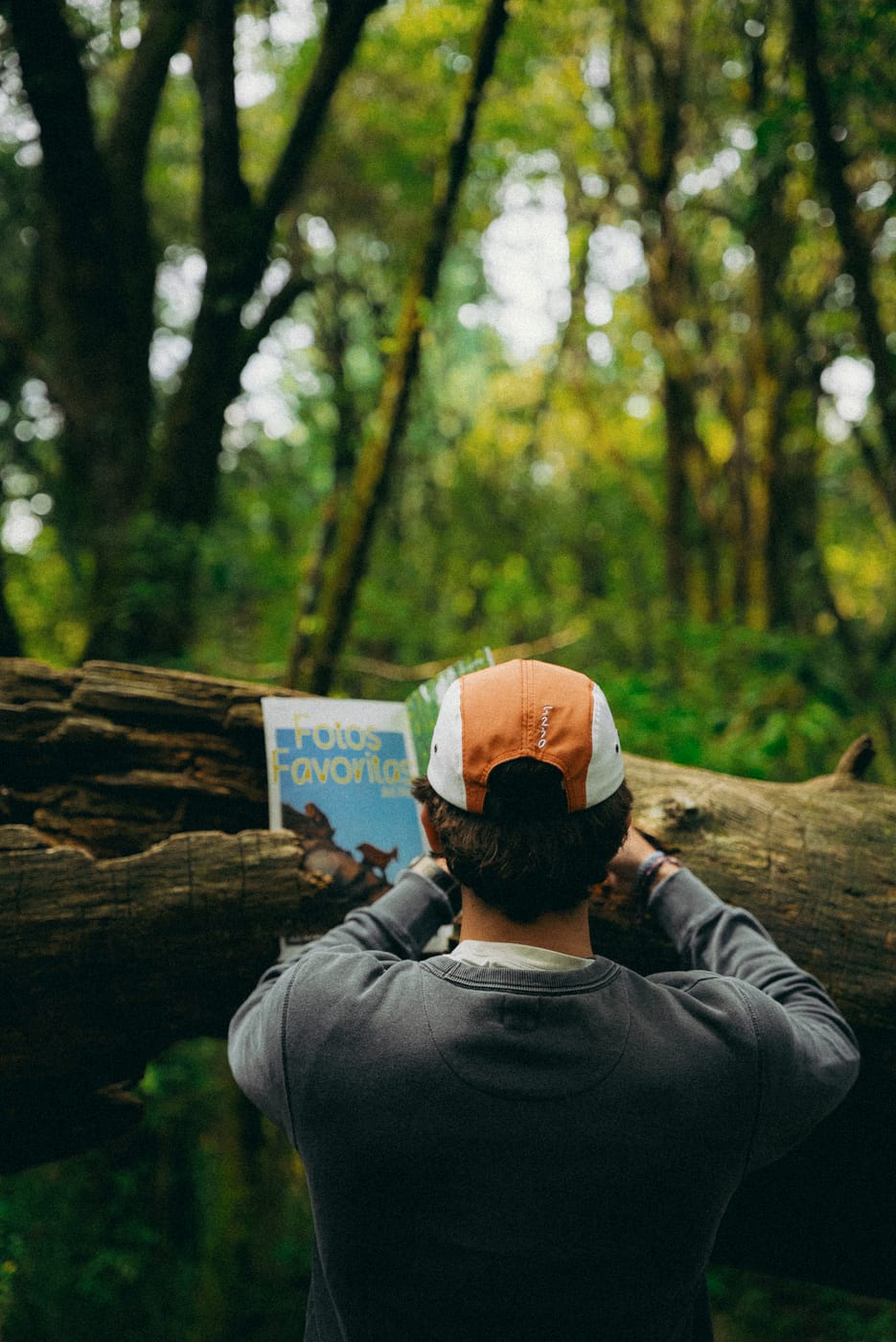 De espaldas frente a un tronco caído, viendo la revista, con la gorra puesta