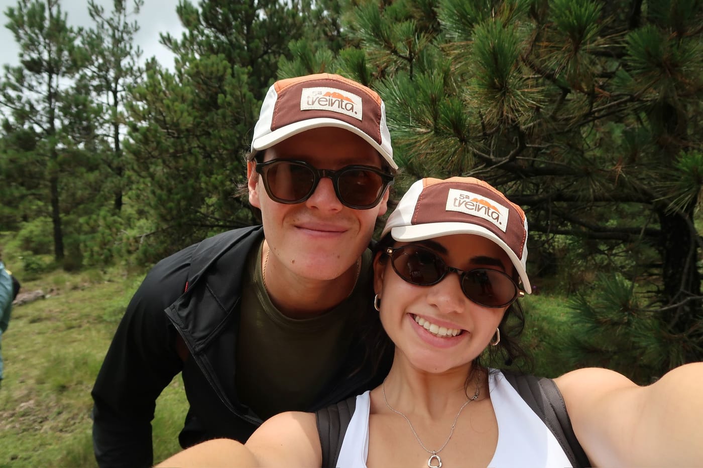 Una selfie de dos entre los pinos, con lentes oscuros y la gorra puesta